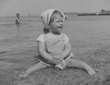 Toddler in a sun suit enjoys sitting in the shallows on a beach Old Photo picture